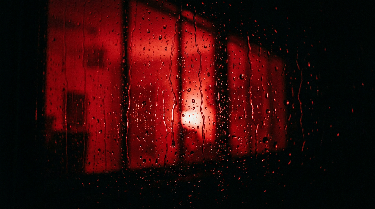 Donker raam met winterse regendruppels, van binnenuit rood verlicht