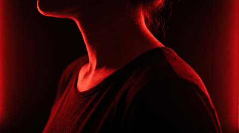 Nek en schouders van opzij in rood licht tegen een zwarte achtergrond