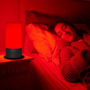 Persoon ligt ontspannen in bed naast een lamp met rood licht