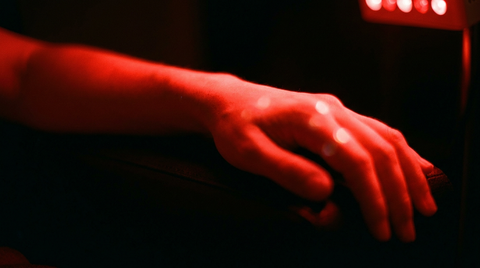 Onderarm en hand met rood licht dat langs de huid strijkt, diepe zwarte achtergrond