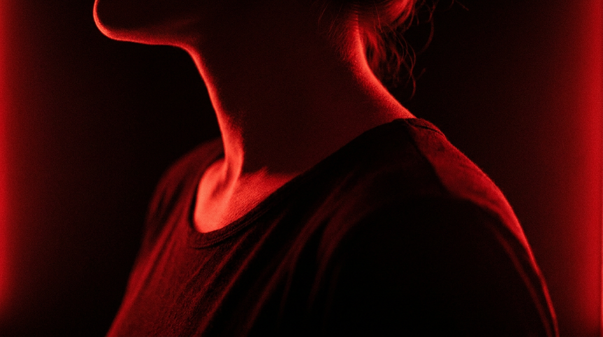 Nek en schouders van opzij in rood licht tegen een zwarte achtergrond