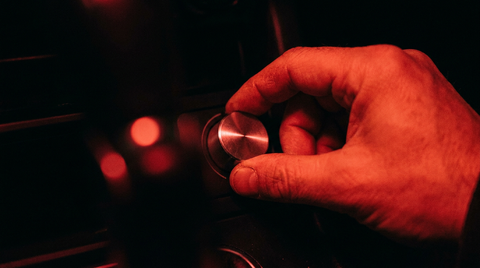 Hand die een ronde draaiknop bedient, verlicht door rood licht tegen een donkere achtergrond