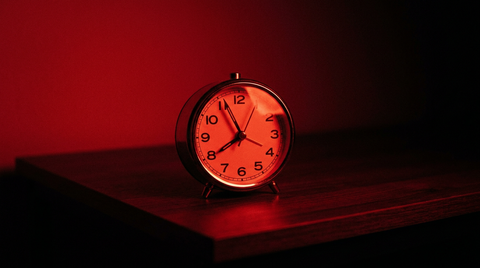 Eenvoudige analoge wekker op een donkere tafel in rood licht